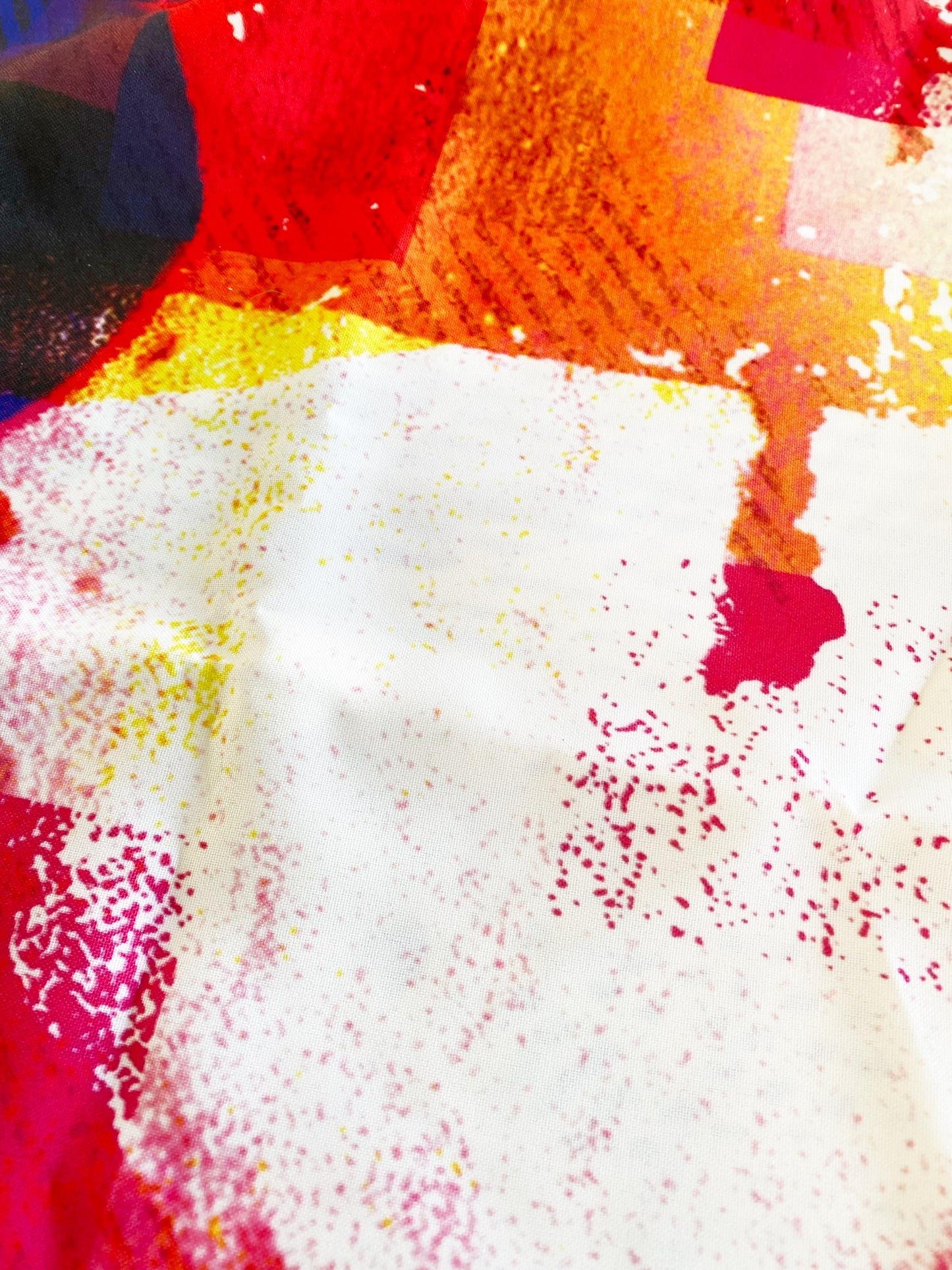 Abstract fabric with red, yellow, and white colors on a textured surface.