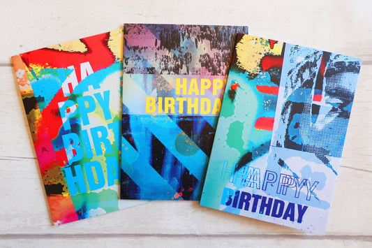 Three colorful birthday cards with abstract designs on a wooden surface