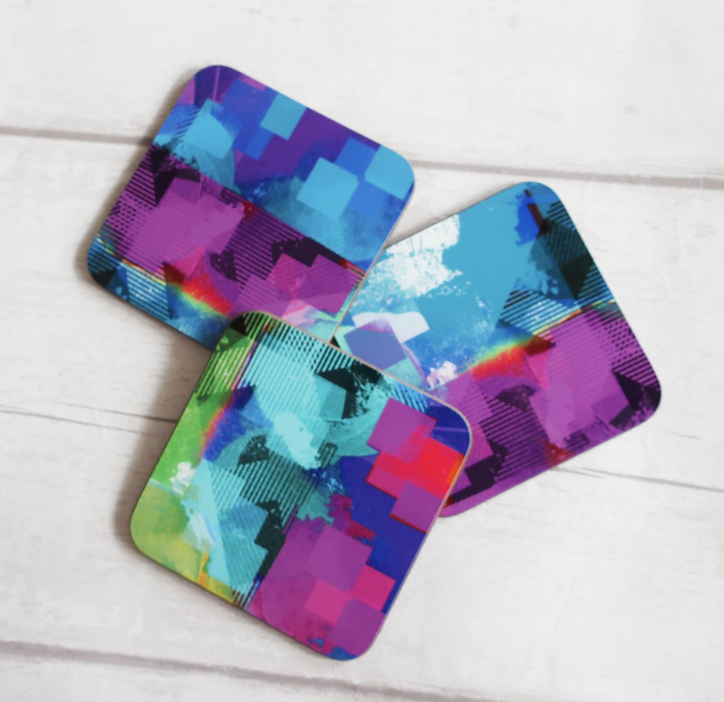 Three colorful abstract patterned coasters on a white wooden surface