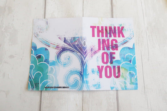 Greeting card with colorful design and 'Thinking of You' text on a wooden surface