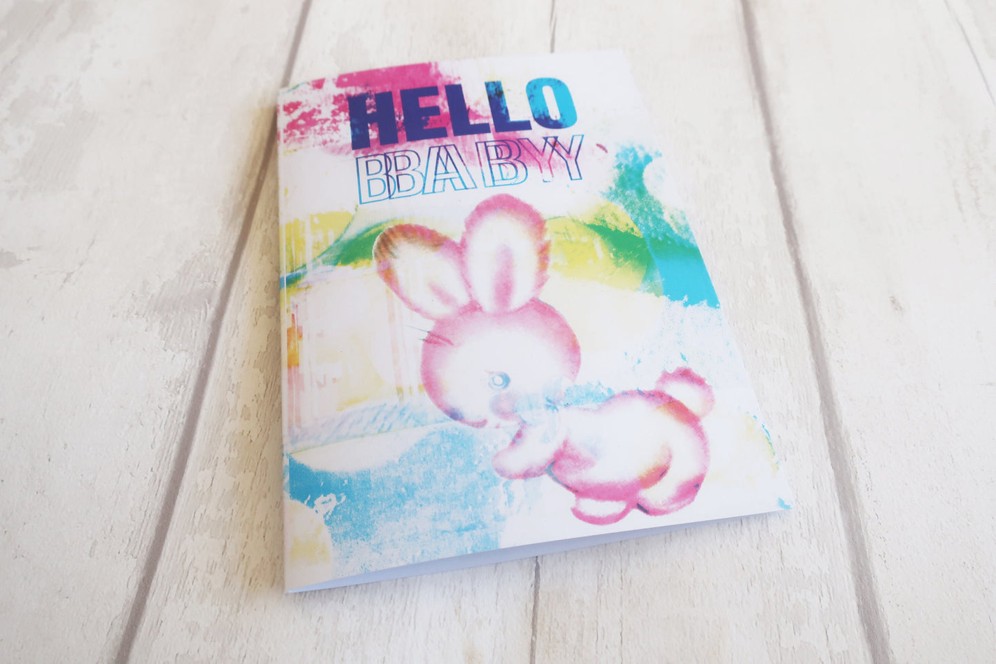 Greeting card with a colorful design of a pink bunny and 'Hello Baby' text on a light wooden surface.