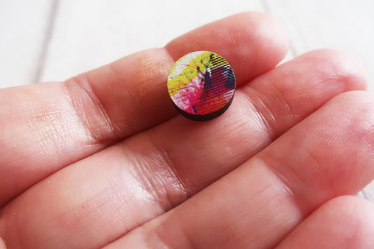 Colorful round earring held between fingers against a white background
