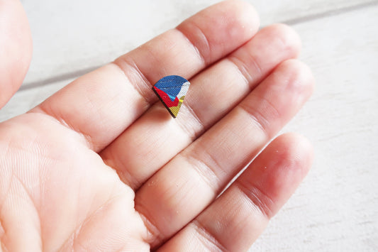 Colorful fan shaped earring held between fingers on a light background
