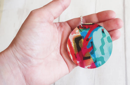 Colorful round pendant held in a hand against a white background