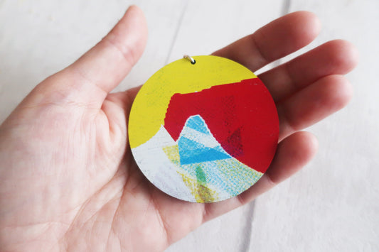 Colorful circular pendant held in a hand against a white background
