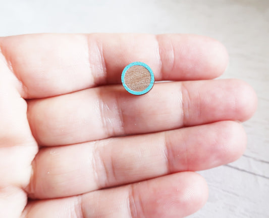 Small round turquoise earring held between fingers on a neutral background
