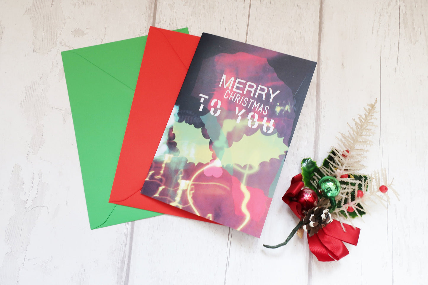 Colorful Christmas card with red and green envelopes on a light wooden surface.
