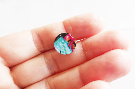 Small round earring with colorful design held between fingers on a white background