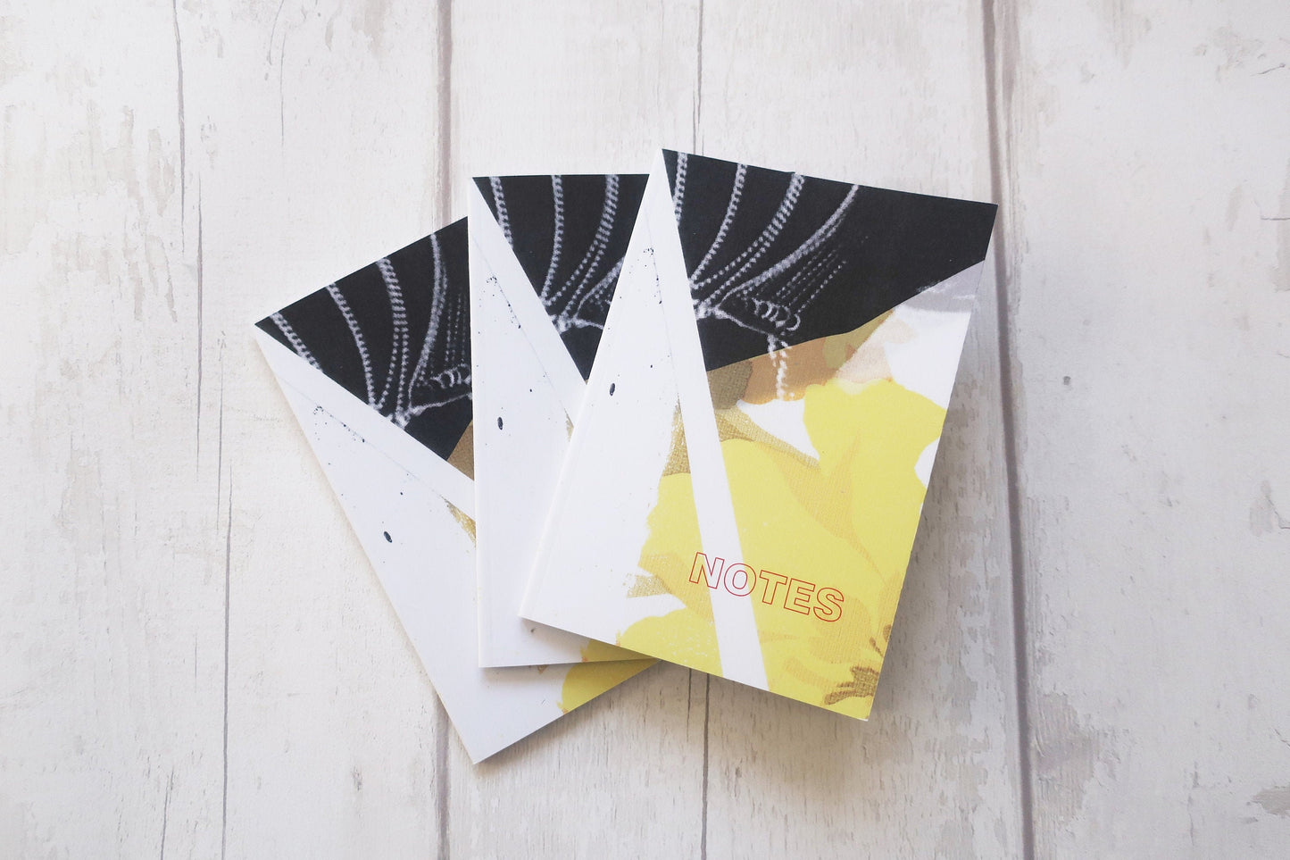 Three notebooks with black and white design on a light wooden surface
