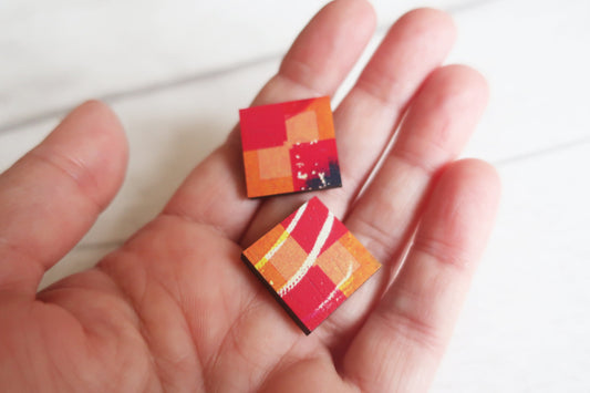 Colorful square earrings held in a hand against a white background