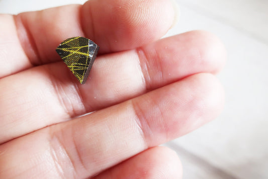 Small geometric earring held between fingers against a neutral background