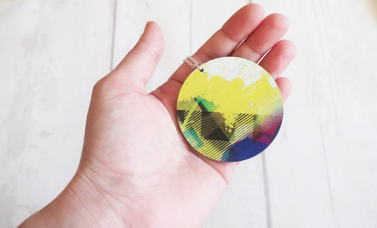 Hand holding a round, multicolored necklace against a white background