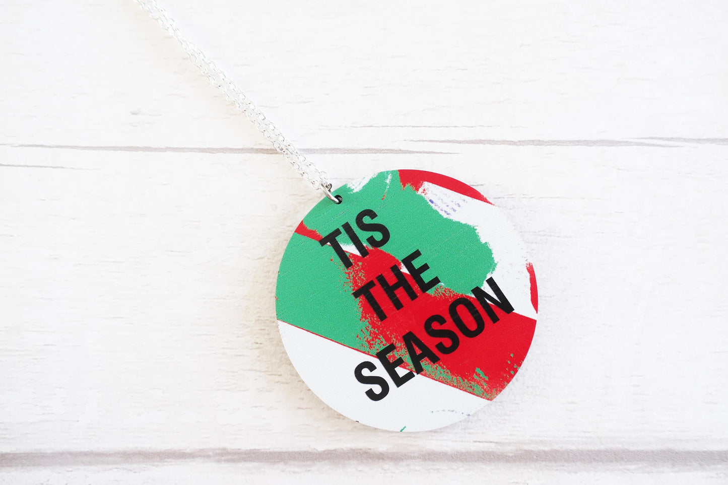 Round decorative necklace with 'Tis the Season' text on a white wooden background