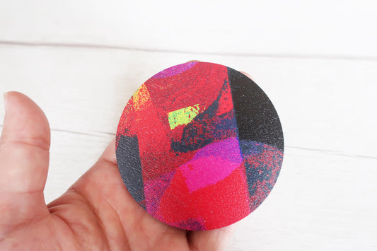 Colorful round brooch held by a hand on a white background
