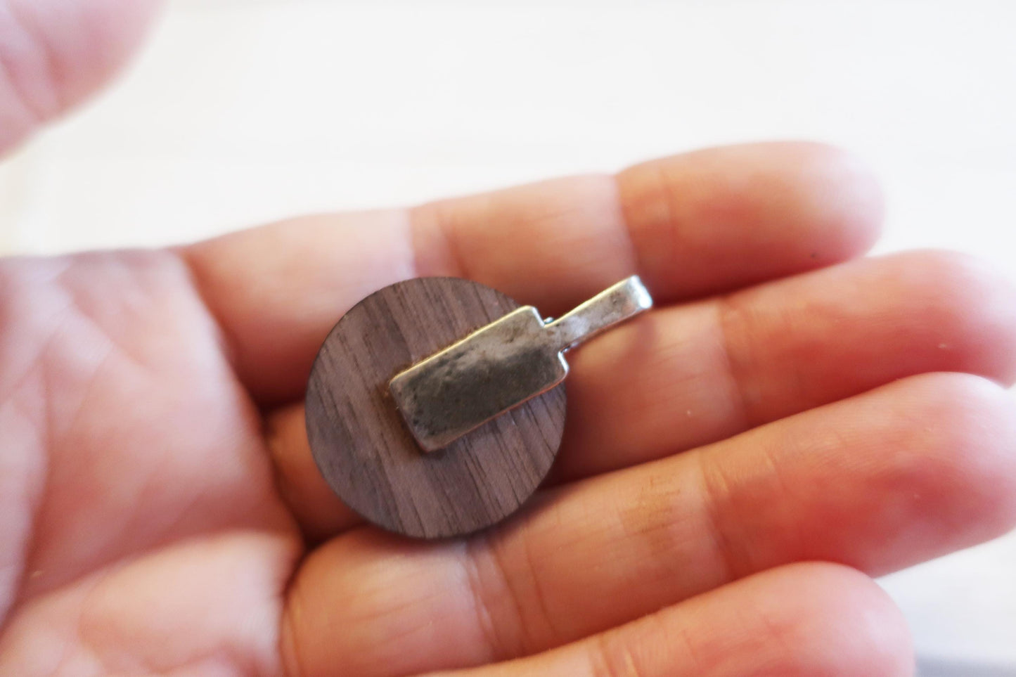Wooden pendant with metal tag held in a hand against a blurred background