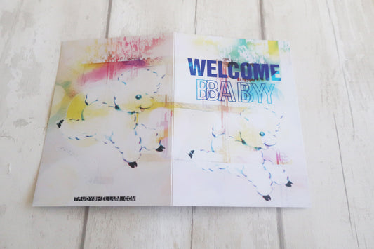 Greeting card with watercolor design and 'Welcome Baby' text on a wooden surface
