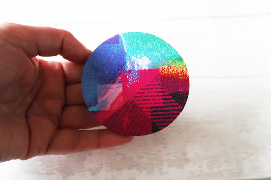 Hand holding a colorful circular brooch with a gradient from blue to red on a light background