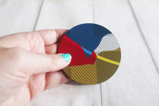 Hand holding a circular brooch with geometric pattern on a light background