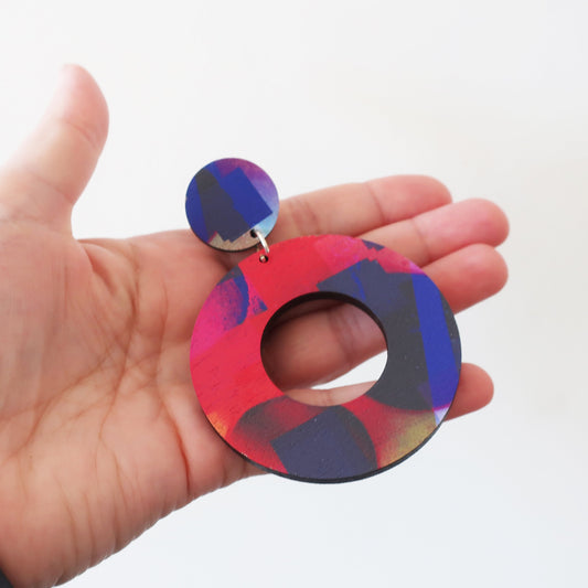 Colorful circular earrings held in a hand against a white background