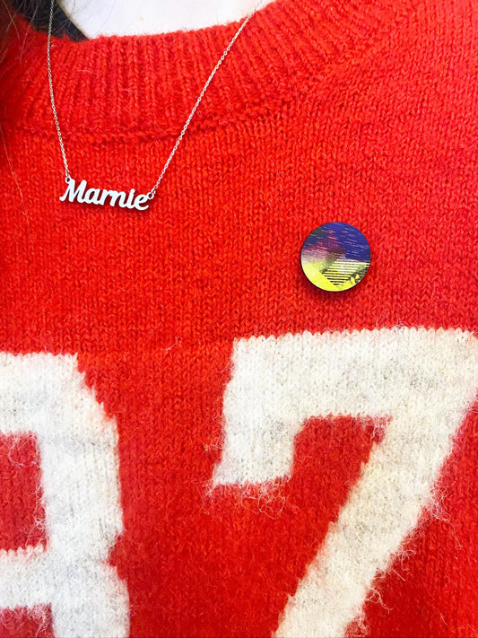 Red sweater with white text and a colorful pin badge, featuring a nameplate necklace.