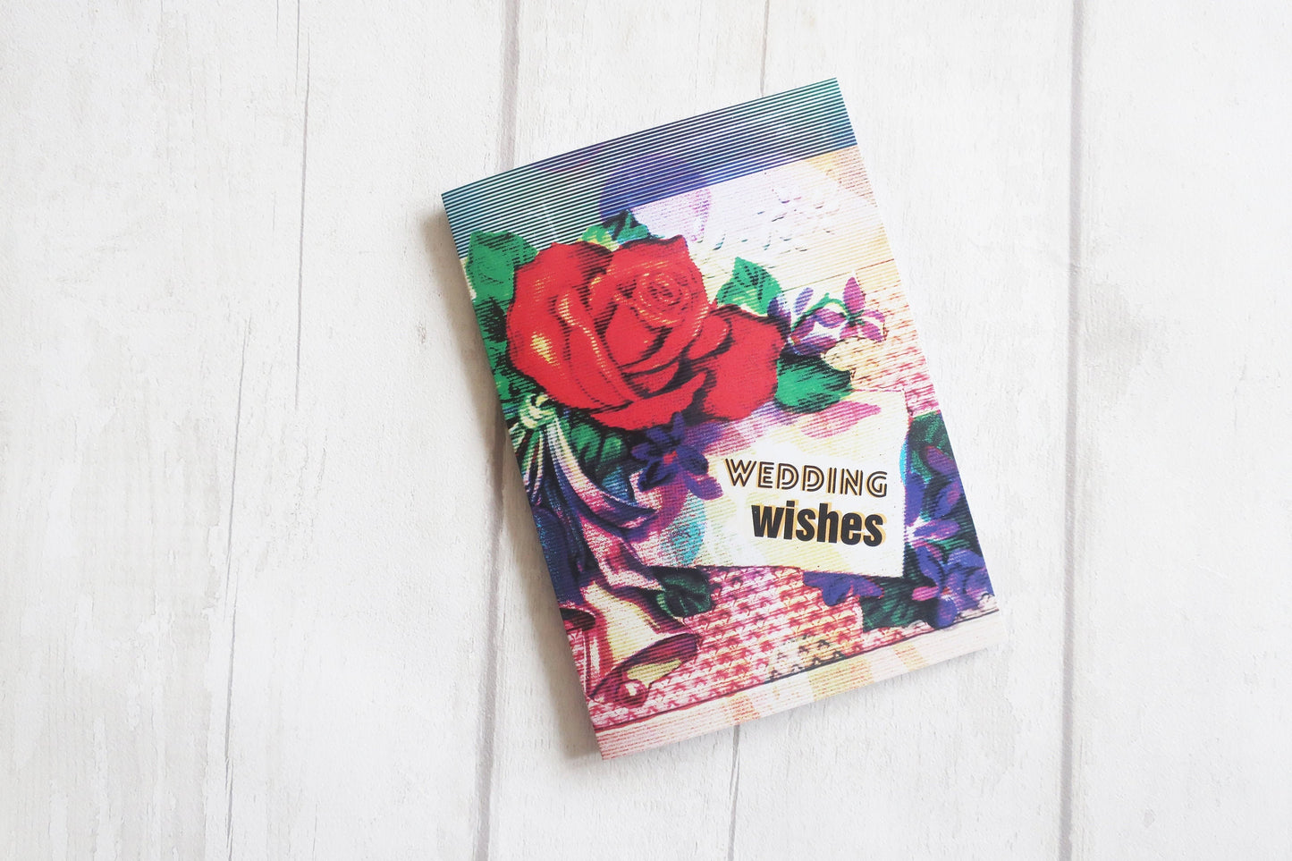 Colorful card with floral design and 'Wedding Wishes' text on a white wooden surface