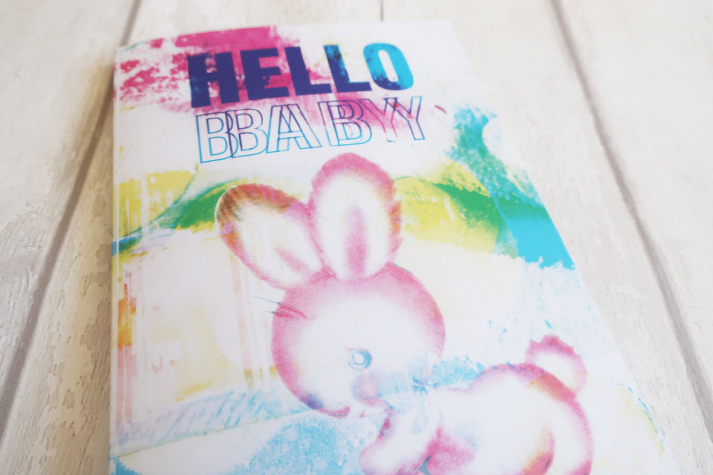 Colorful Greeting card with a rabbit illustration and 'HELLO BABY' text on a light wooden surface.