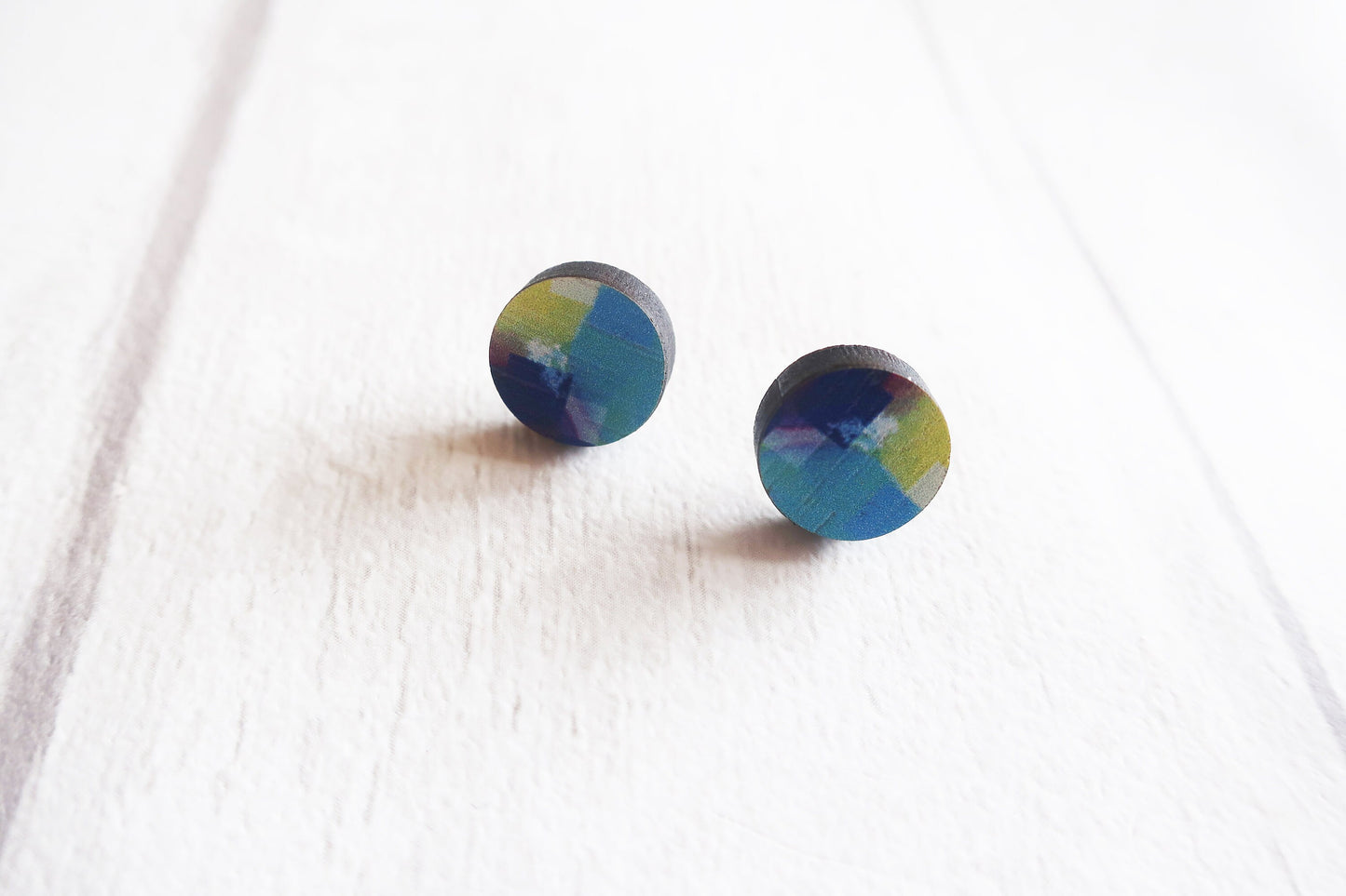 Pair of round earrings with a multicolored design on a white fabric background