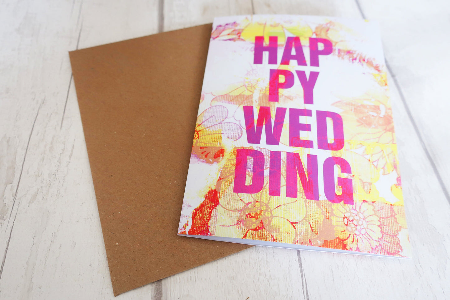 Colorful wedding card with floral design and 'Happy Wedding' text on a wooden surface.
