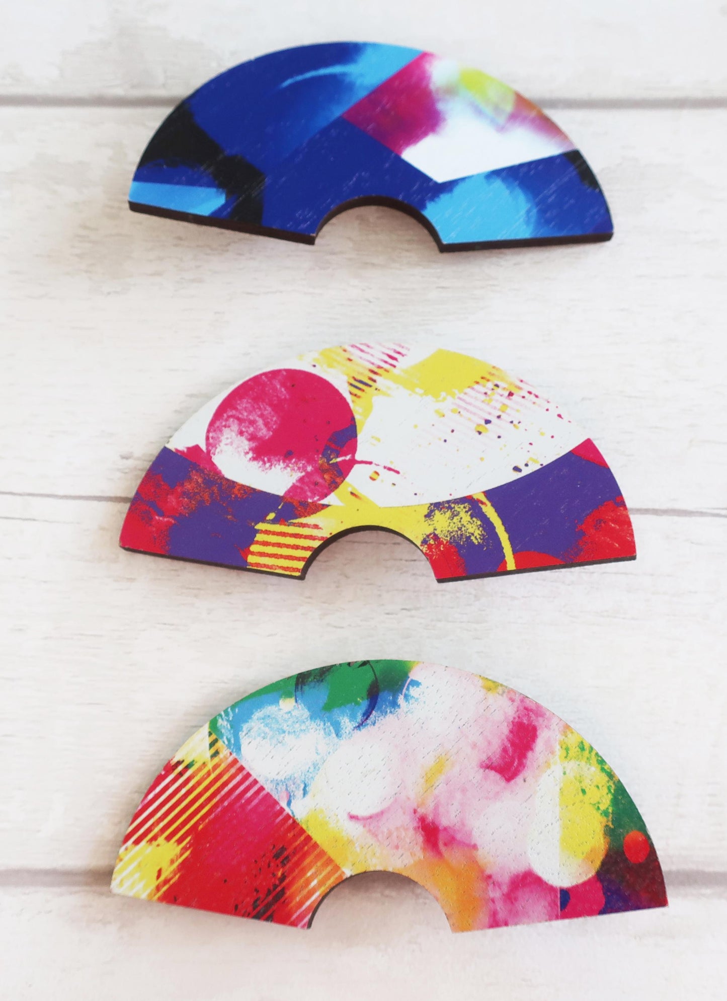 Three colorful half-circle hairclips on a light wooden surface