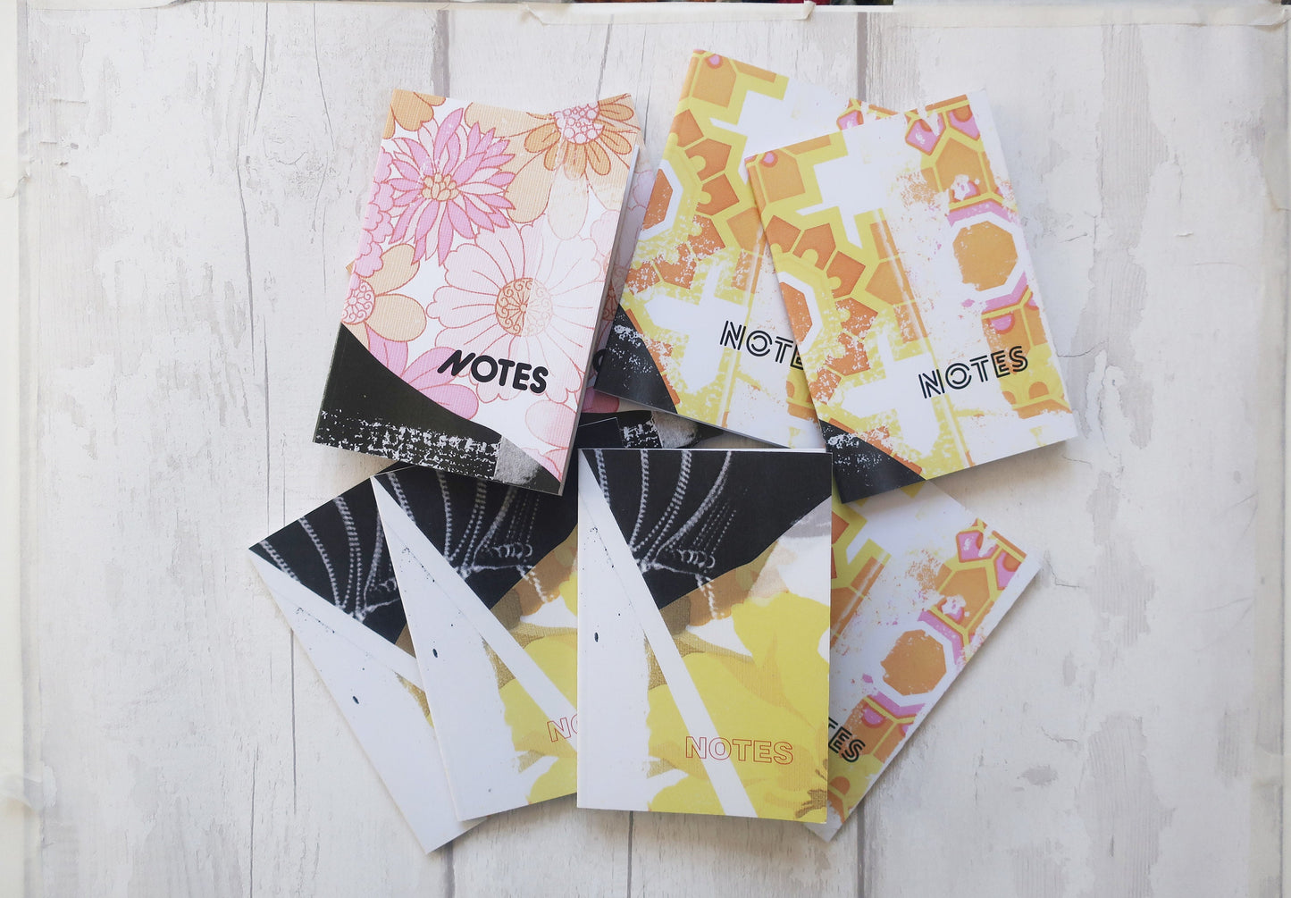 Small notebooks with colorful designs and 'NOTES' text on a light wooden surface
