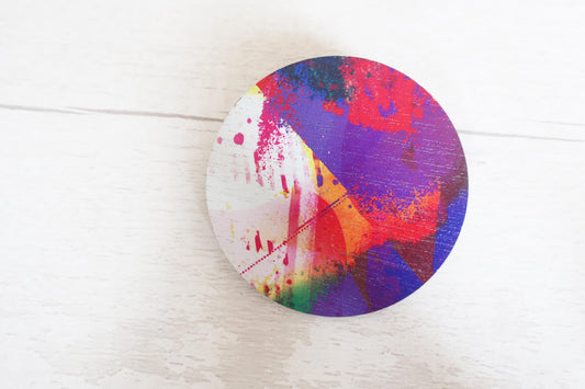 Colorful abstract brooch on a circular object against a white background