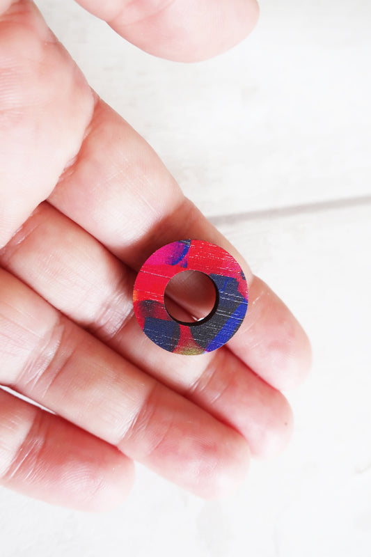 Colorful circular earring held between fingers on a white background