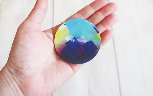 Hand holding a round, multicolored pendant against a white background