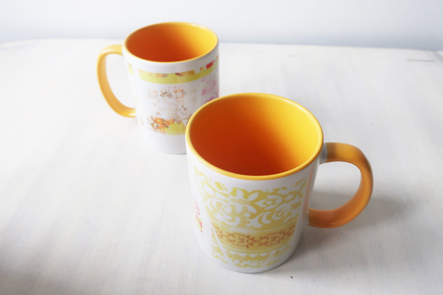 Two mugs with yellow interiors and handles on a white surface