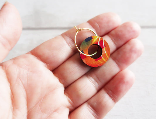 Colorful hoop earring held in a hand against a light background