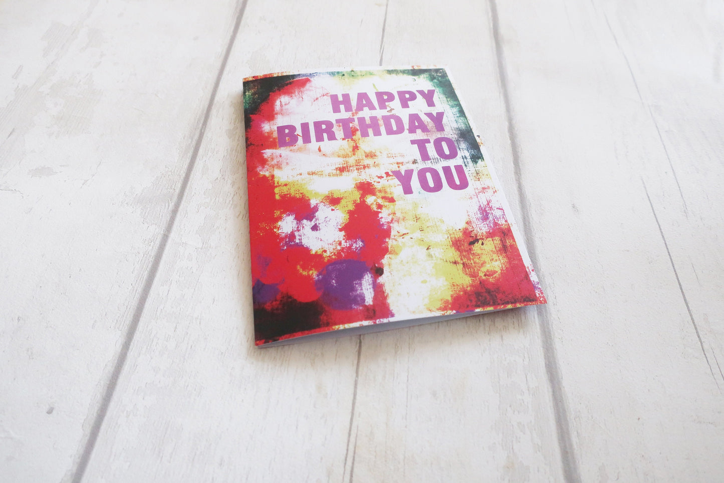 Colorful birthday card with 'Happy Birthday To You' text on a white wooden surface