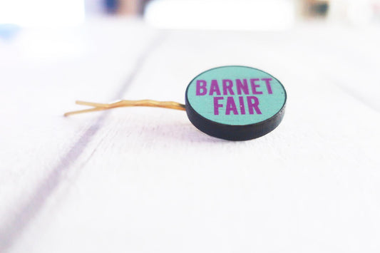 Round hair clip with 'Barnet Fair' text on a white background