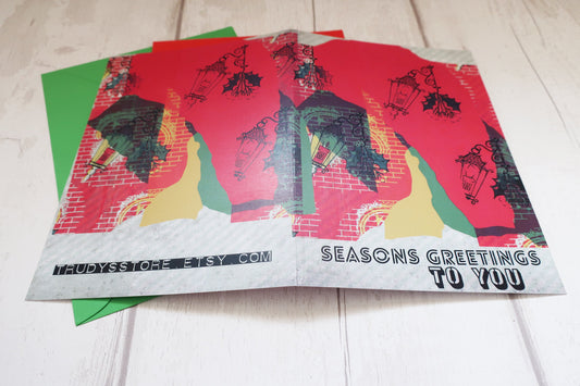 Stack of greeting cards with artistic designs and 'Seasons Greetings To You' text on a light wooden surface.