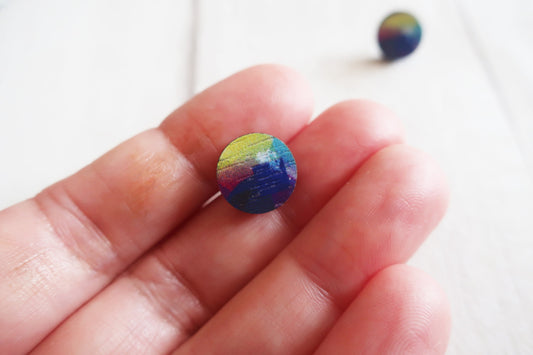 Multicolored round earring held between fingers against a white background