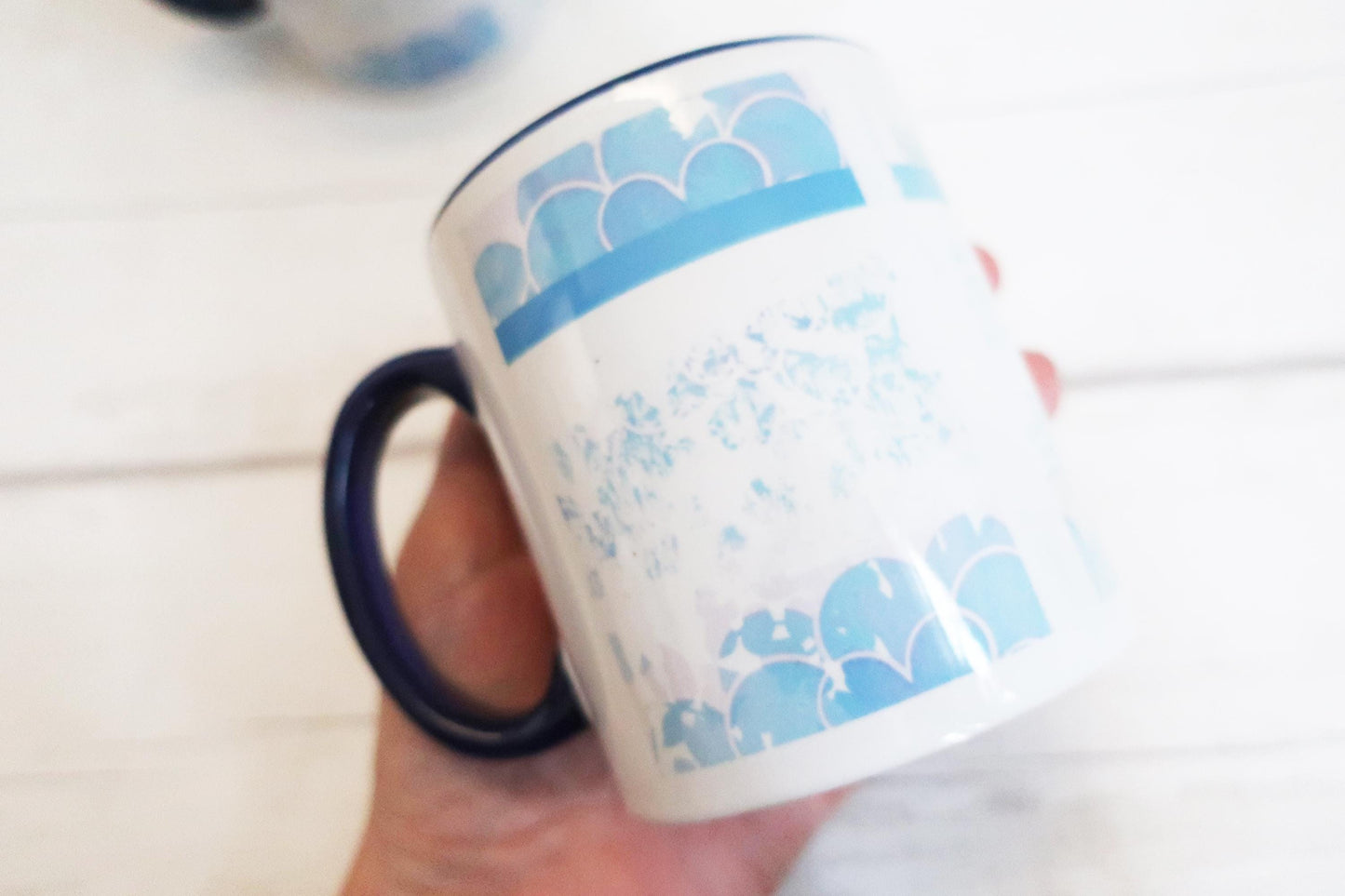 Mug with blue pattern held by a hand on a white surface
