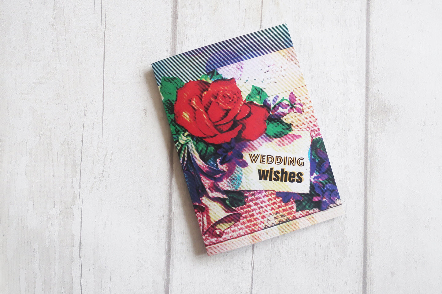 Colorful wedding card with floral design and 'Wedding Wishes' text on a white wooden surface