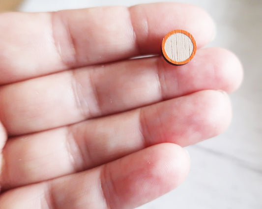 Small round earring with a wooden texture held between fingers on a neutral background