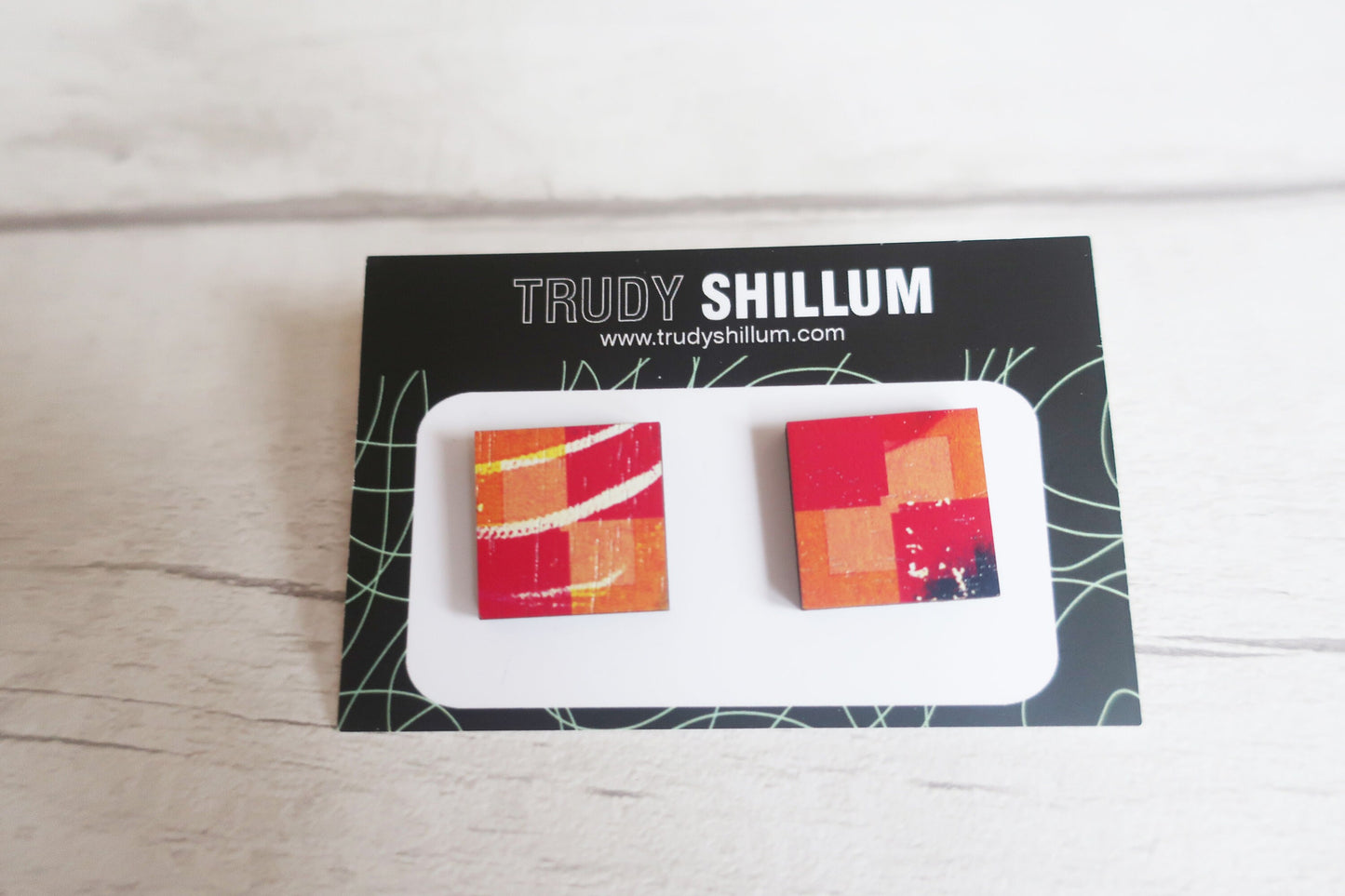 Colorful square earrings on a Trudy Shillum branded card against a light wooden background