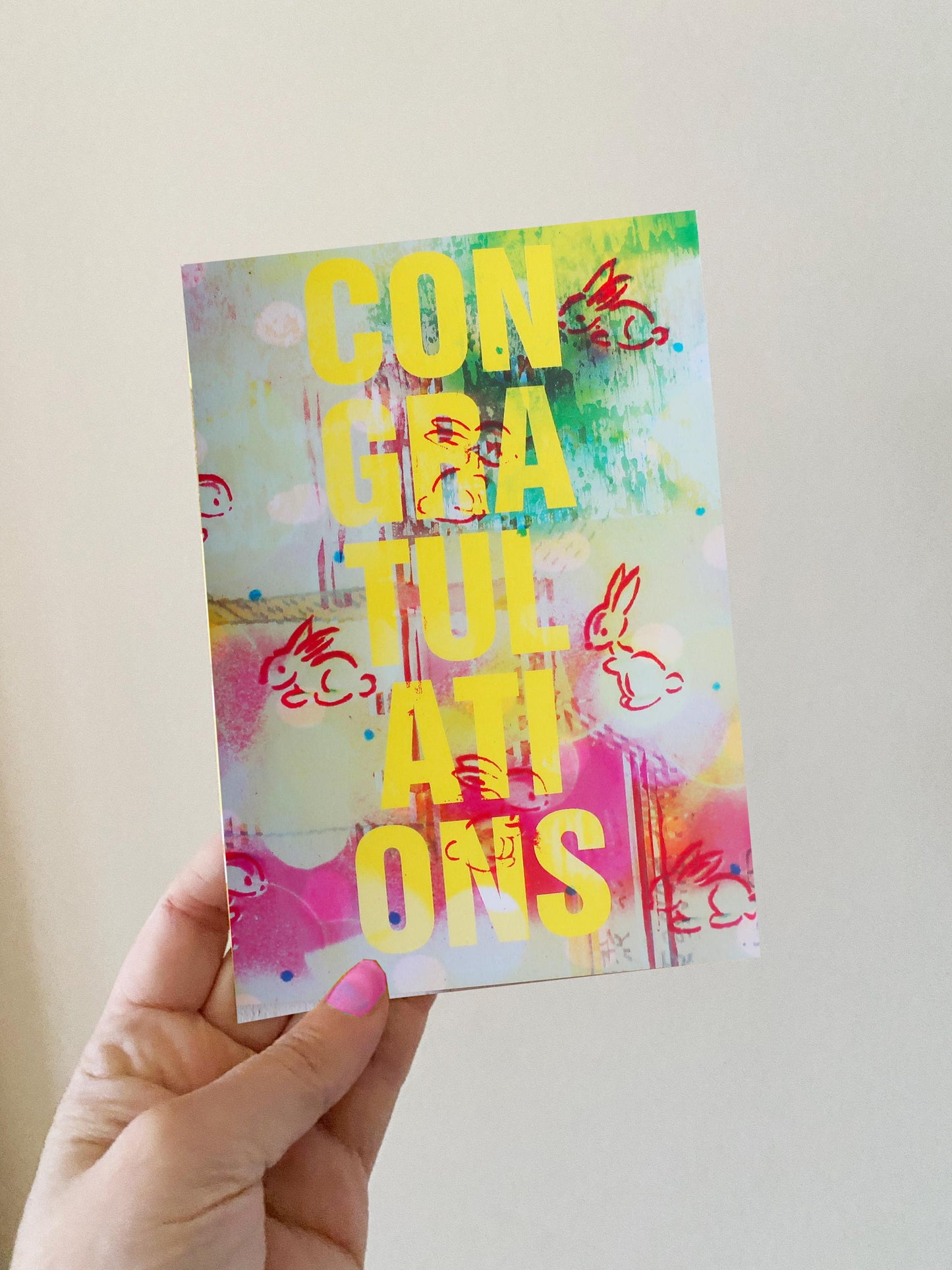 Hand holding a colorful card with 'Congratulations' text against a plain background