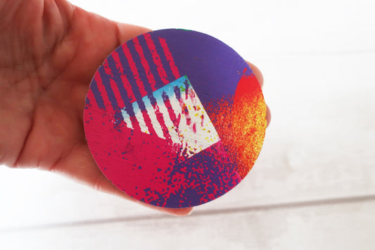 Colorful circular brooch with abstract design held by a hand on a white background