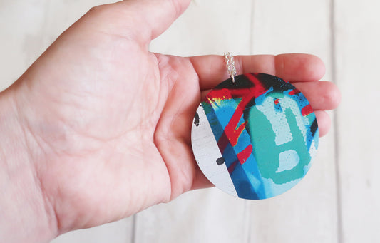 Hand holding a colorful round pendant against a plain background