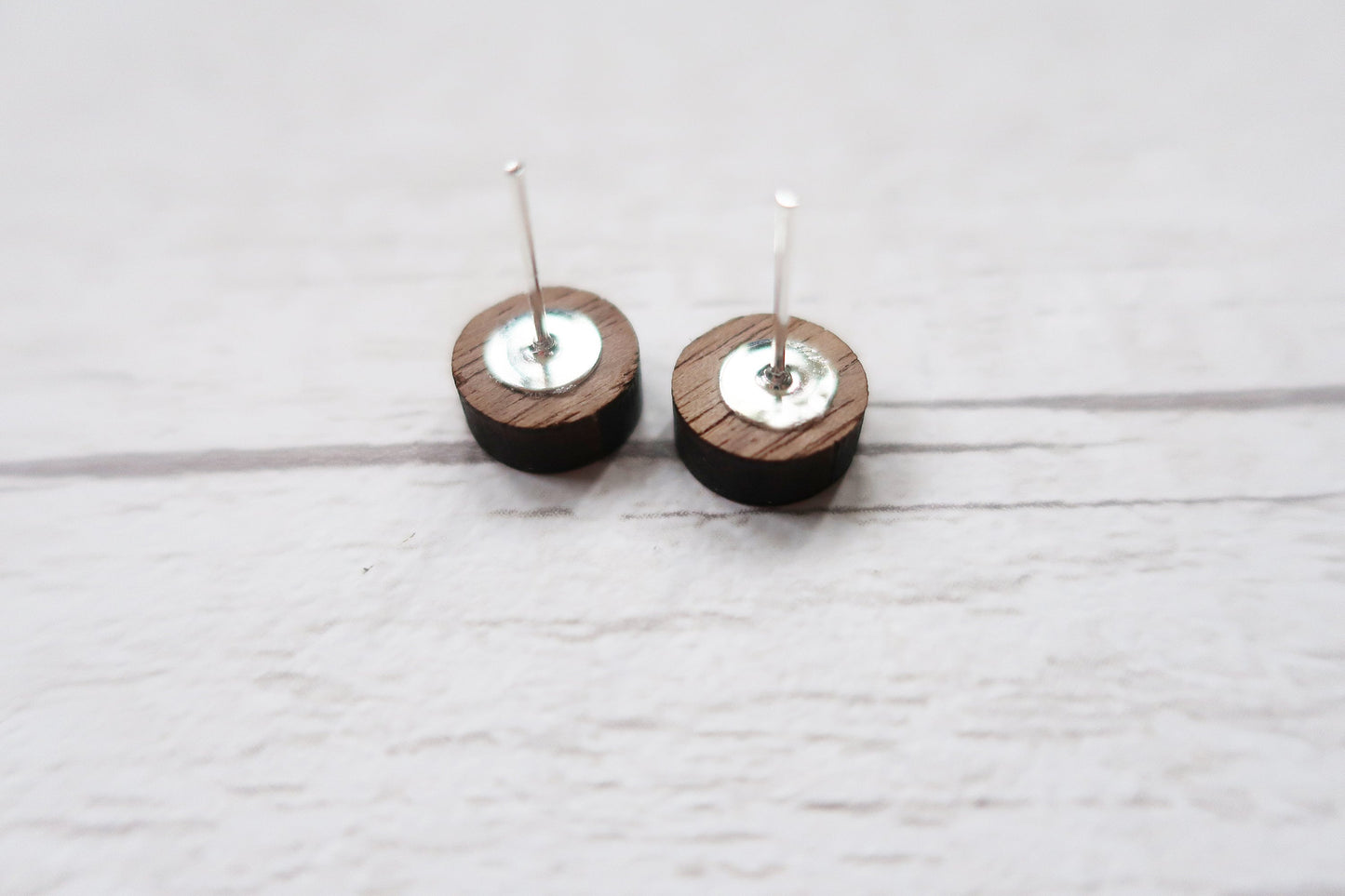 Pair of wooden earrings with silver tops on a light gray background