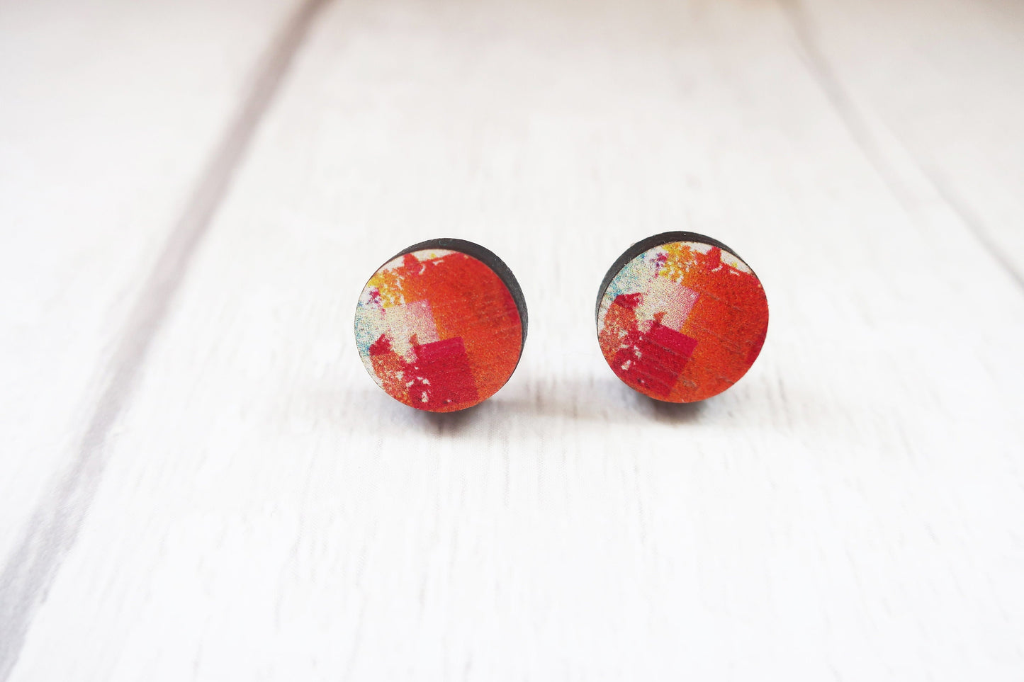 Pair of round earrings with red and white design on a white background