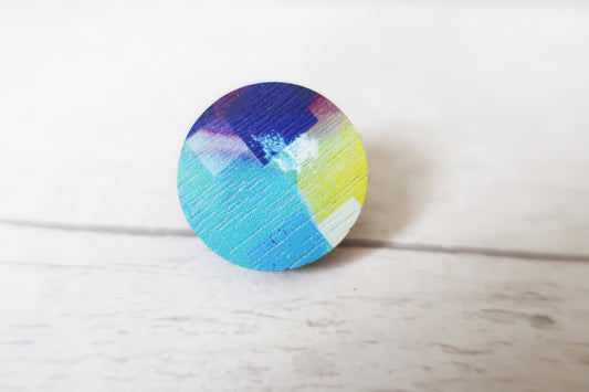 Round wooden pin badge with colorful design on a light wood surface