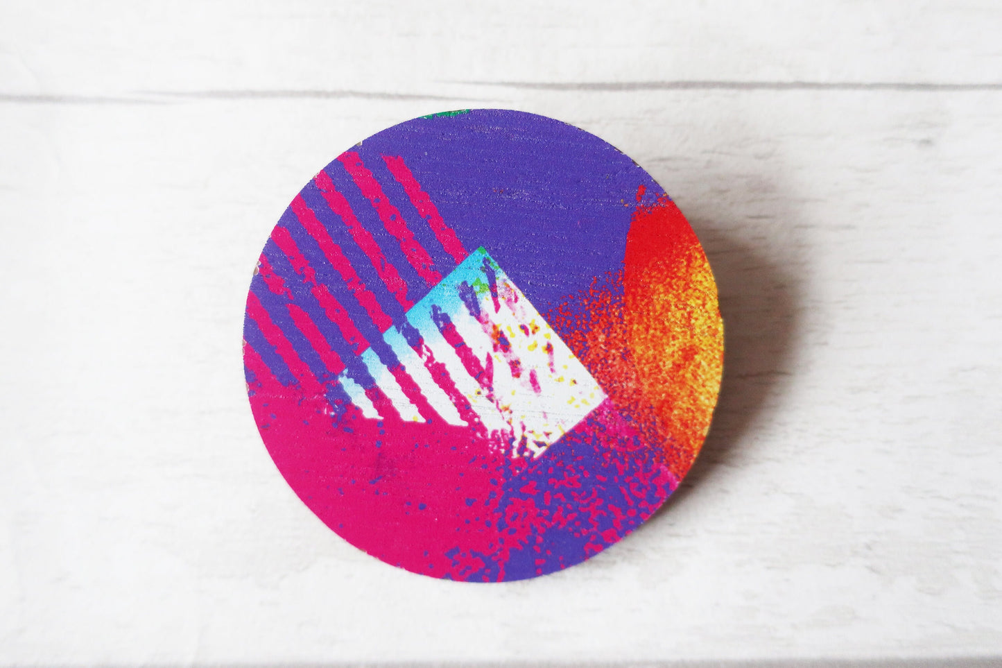 Colorful circular brooch with abstract design on a white background